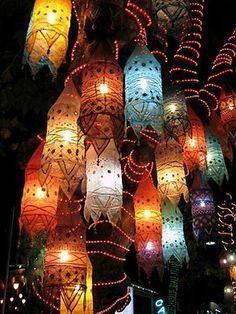 many colorful lanterns are hanging from the ceiling in front of trees and buildings at night