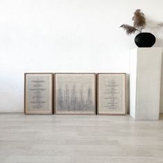 three framed art pieces sitting on top of a hard wood floor next to a vase