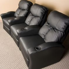 three black recliners sitting next to each other on the floor in front of a wall