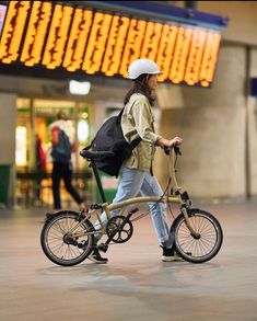 a person with a backpack is riding a bike in an airport terminal, while wearing a white helmet and carrying a black bag