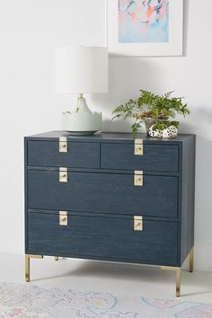 a blue dresser with brass handles and drawers in a white room next to a painting on the wall