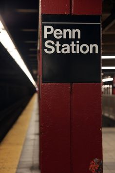 a sign that is on the side of a red wall in a subway station next to a platform