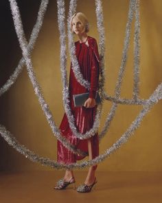 a woman in a red dress standing next to silver trees