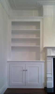 an empty living room with white painted walls and fireplace in the corner, along with built - in shelving