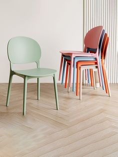 four different colored chairs sitting next to each other on a hard wood floor in front of a white wall