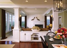 a dining room table and chairs in front of a kitchen with white cabinets, wood floors and an open fireplace