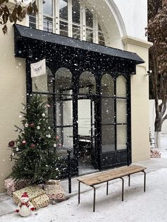 a small christmas tree in front of a building with snow falling on the ground around it