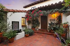 an outdoor patio with potted plants and flowers on the side of the house at dusk