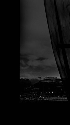 a black and white photo of a window with mountains in the background at night time