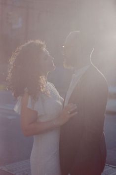 a man and woman standing next to each other in front of a building with the sun shining on them