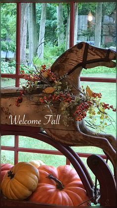 a rocking horse with pumpkins and gourds in front of a welcome fall sign