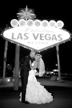 a bride and groom kissing in front of the welcome to las vegas sign at night