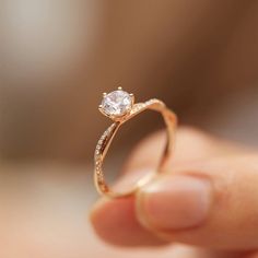 a close up of a person's hand holding a ring with a diamond on it