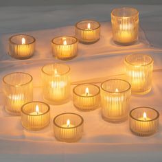 many lit candles are arranged on a white cloth