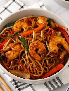 a white bowl filled with shrimp and veggies next to chopsticks on a table