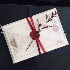 an open envelope with a red ribbon tied around it and some flowers on the inside