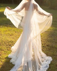 a woman in a wedding dress with her arms spread out to show the back of her veil