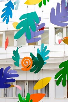 multicolored paper cutouts hanging from the ceiling in front of a white building