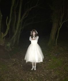 a woman in a white dress standing in the woods at night with her hands on her face