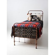 an old iron bed with a plaid blanket on it