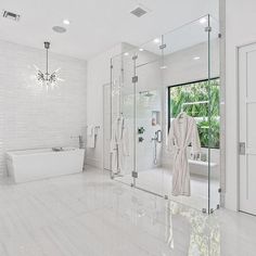 a white bathroom with glass walls and large tub in the center, surrounded by marble flooring