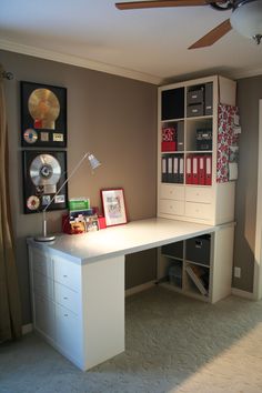 a room with a white desk and some pictures on the wall next to a ceiling fan