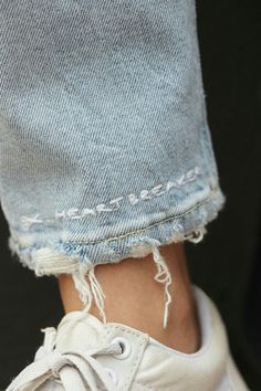 a person's foot with white sneakers and ripped jeans