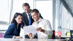 two men and a woman looking at a piece of paper