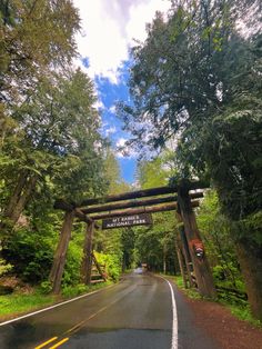 the entrance to an open road surrounded by trees and greenery, with a sign above it