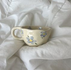 a white cup with blue and yellow flowers on it sitting on top of a bed