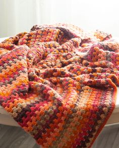 a crocheted blanket sitting on top of a white bed next to a window