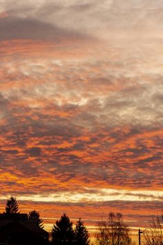 the sky is red and orange as the sun sets in the distance behind some trees