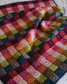 a multicolored blanket laying on top of a white tablecloth covered in crochet