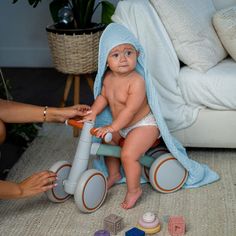 a baby in a blue towel sitting on top of a tricycle next to toys