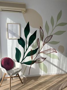 a white chair sitting in front of a wall with green leaves painted on the side