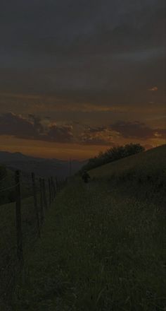 the sun is setting over a grassy hill with a fence and trees in the foreground