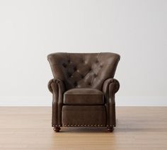 a brown leather chair sitting on top of a hard wood floor next to a white wall