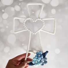 a hand holding a crocheted cross ornament with blue flowers on it