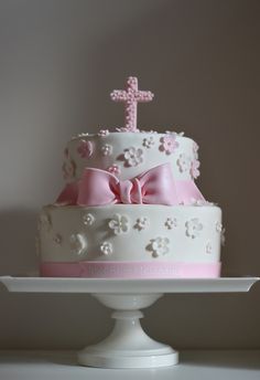 a white cake with pink bows and a cross on top