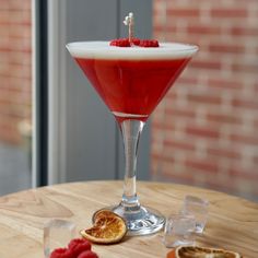 a glass filled with red liquid sitting on top of a wooden table