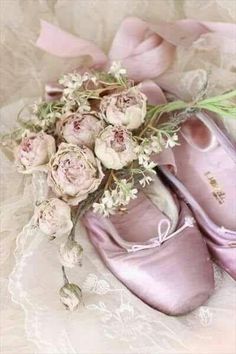 two pairs of ballet shoes with flowers in them on a lace doily next to a bouquet of pink roses