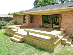 a wooden deck in front of a brick house with steps leading up to the patio