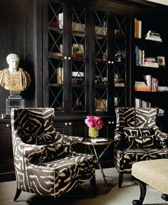 two zebra print chairs in front of a bookcase with a vase on the table