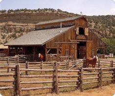 two horses standing in front of a barn with mountains in the background and brown grass on the ground