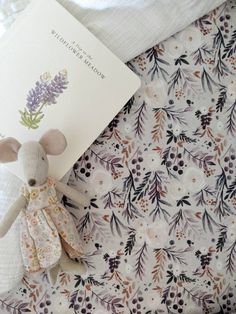 a small stuffed animal next to a book on a floral print bed spread with white linens