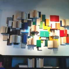 an art piece made out of books on the wall above a book shelf with several different colored books