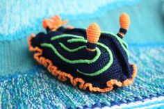 a close up of a crocheted animal on a blue and green blanket with orange accents