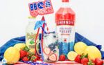 a basket filled with fruit and drinks on top of a blue cloth covered tablecloth