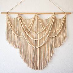 macrame wall hanging with beads and wooden dows on a white wall background