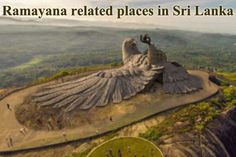 a large bird statue sitting on top of a lush green hillside next to a forest